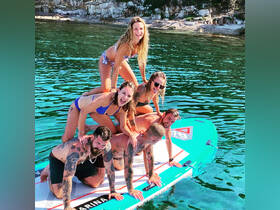 A lively group of friends balances on a paddleboard in crystal-clear waters, showcasing the fun and excitement of summer adventures on the water.