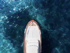 Aerial view of a sleek yacht gliding over crystal-clear waters, showcasing the beauty of boating adventures in stunning marine environments.