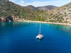A stunning aerial view of a catamaran anchored in crystal-clear waters, surrounded by picturesque hills and a serene beach, perfect for a relaxing getaway.