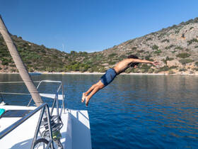 A man leaps off the side of a catamaran into the crystal-clear waters, capturing the thrill of summer adventures on the water.