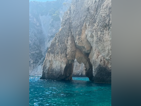 A stunning view of a natural rock formation arching over crystal-clear waters, showcasing the breathtaking coastline — perfect for scenic boat tours.