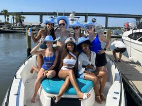 A lively group of friends poses on a boat, celebrating with fun hats and drinks — perfect for a day out on the water.