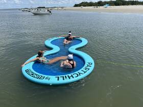 A fun group enjoys a sunny day on a floating mat in shallow waters, perfect for relaxation and socializing during a beach outing.