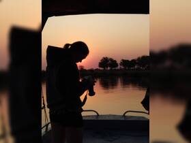 A silhouette of a person capturing the sunset from a boat, creating a serene moment perfect for photography enthusiasts and nature lovers.