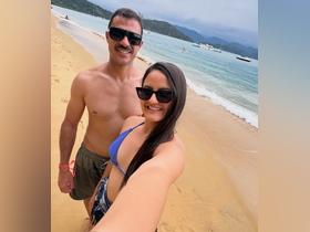 A cheerful couple takes a selfie on the beach, enjoying their vacation with beautiful waters in the background — a perfect moment of relaxation and fun.