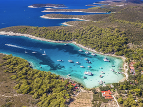 A stunning aerial view of a picturesque harbor surrounded by lush greenery and crystal-clear waters, showcasing various boats anchored in a serene bay — perfect for island hopping adventures.