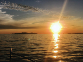 A serene sunset view over calm waters, with distant islands silhouetted against the vibrant sky — an ideal scene for peaceful evening boat cruises.