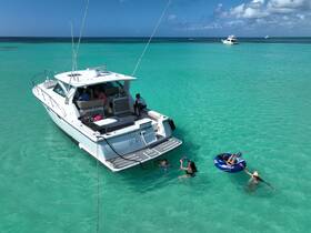 A lively group enjoys a fun day on the water, swimming and tubing near a stylish boat in stunning turquoise waters — perfect for summer adventures.