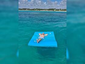 A man relaxes on a floating mat in the crystal-clear ocean, enjoying a perfect day of sunbathing and tranquility.