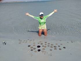 A joyful woman celebrates at the beach, surrounded by sand dollars and shallow water — a perfect moment of fun in the sun.