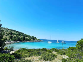A picturesque view of sailboats anchored in turquoise waters, framed by lush greenery and a serene coastline — an ideal destination for sailing enthusiasts and nature lovers.