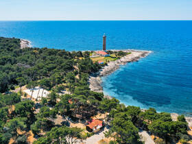 A stunning aerial view of a picturesque coastline featuring a historic lighthouse surrounded by lush greenery and clear blue waters, perfect for exploring scenic destinations.