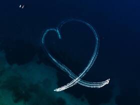 An aerial view captures boats creating a heart shape in the deep blue waters, showcasing a playful on-water activity perfect for romantic outings or celebrations.