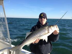 A proud angler holds up a freshly caught striped bass while fishing on the open ocean — a perfect capture of the thrill of sport fishing.