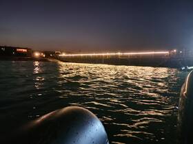 A nighttime view of a pier illuminated by lights, with reflections on the water. The image lacks clarity and detail.