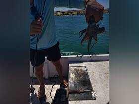 A fisherman proudly holds up a freshly caught octopus on a boat, showcasing the thrill of a successful fishing trip.
