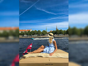 A woman relaxes on the deck of a boat, enjoying a scenic view of the city skyline and water activities — a perfect moment for leisure on the water.
