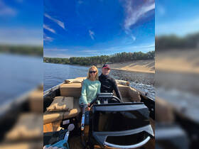A couple enjoys a scenic day on the water, with one at the helm of a stylish boat, perfect for romantic outings or adventurous explorations.
