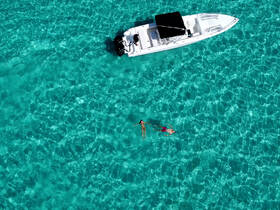 A couple enjoys a refreshing swim in crystal-clear waters, with a boat anchored nearby, perfect for a day of fun and relaxation on the water.