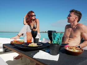A couple enjoys a delightful meal on a boat, surrounded by stunning turquoise waters — perfect for a relaxing day on the water.