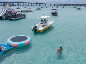 A lively scene featuring people enjoying water activities, including swimming and lounging on a floating trampoline, with boats anchored in the background — perfect for a fun day on the water.