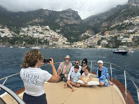 A family poses for a photo on a boat with the picturesque town of Positano in the background, showcasing the beauty of the Amalfi Coast — a perfect moment captured during their tour.