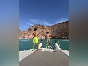 Two boys enjoy the view from the bow of a boat, overlooking a beautiful beach and rocky landscape — a perfect moment for adventure and exploration.