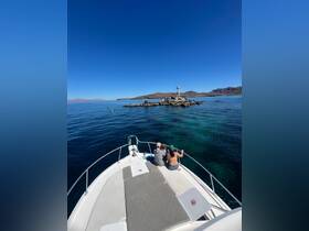 A couple enjoys the stunning view from the bow of a boat, overlooking a picturesque island with a lighthouse — a perfect moment for adventure seekers and nature lovers.