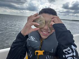 A joyful child playfully holds sand dollars over their eyes while enjoying a boat trip, capturing the essence of fun and adventure on the water.