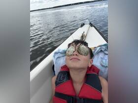 A child enjoys a playful moment on a boat, using shells as sunglasses while soaking up the sun — a delightful snapshot of summer fun on the water.