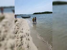Two children enjoy a sunny day at the beach, playing in the water near a boat — a perfect family outing for summer fun.