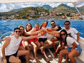 A lively group of friends celebrates on a boat, raising cocktails against a stunning coastal backdrop — perfect for unforgettable summer outings.