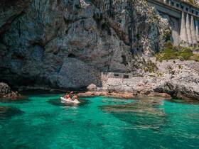 Two kayakers paddle through crystal-clear waters, exploring a stunning coastline with rocky cliffs — an ideal adventure for nature lovers.