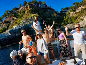 A joyful group of friends and family celebrate on a boat, enjoying the sun and each other's company against a stunning coastal backdrop.