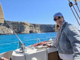 A woman enjoys a sunny day sailing on a boat, with stunning cliffs and turquoise waters in the background — perfect for adventure seekers and nature lovers.