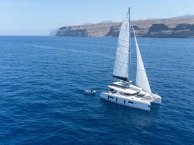 A stunning aerial view of a catamaran sailing through deep blue waters, showcasing the vessel's sleek design against a picturesque coastal backdrop.