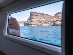 A serene view from inside a boat's cabin, showcasing a rocky coastline through the window — perfect for those seeking tranquility on the water.