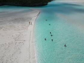 Aerial view of a stunning beach scene with people enjoying the crystal-clear waters, perfect for island hopping adventures and relaxing days in paradise.