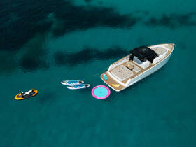An aerial view of a luxury boat anchored in crystal-clear waters, featuring a jet ski, paddleboards, and a floating mat, perfect for a day of fun on the water.