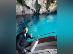 A man gives a thumbs up aboard a boat in a stunning cave with turquoise waters, capturing the excitement of a unique boating adventure.