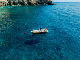 A scenic view of a boat anchored in crystal-clear waters with a swimmer nearby, showcasing the beauty of coastal adventures and water activities.