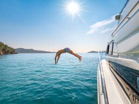 A person leaps off the side of a boat into the sparkling blue ocean, capturing the essence of summer fun and adventure on the water.