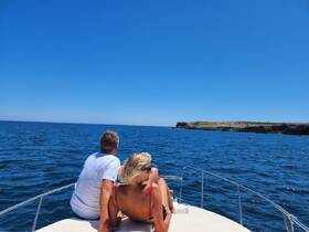 A couple enjoys a serene moment on the bow of a boat, gazing at the beautiful ocean scenery — perfect for romantic getaways or peaceful excursions.