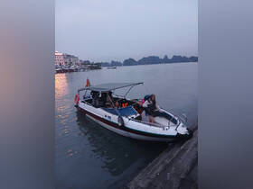 A group of people boards a boat at dusk, with scenic mountains in the background, capturing the essence of an evening adventure on the water.