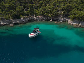 A stunning aerial view of a yacht anchored in crystal-clear turquoise waters, surrounded by lush greenery — perfect for serene getaways and island explorations.