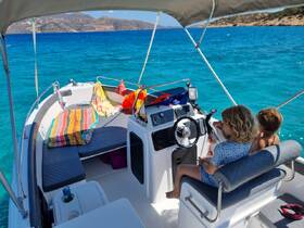 Two children enjoy a moment at the helm of a boat, surrounded by colorful towels and the stunning turquoise waters — a perfect setting for family adventures on the sea.
