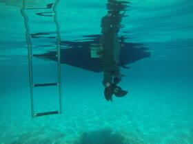 Underwater view of a boat's propeller and ladder, showcasing the vessel's structure beneath the crystal-clear water.