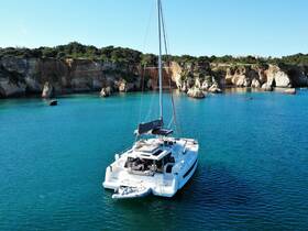 A stunning aerial view of a catamaran anchored in crystal-clear waters, surrounded by picturesque cliffs — perfect for exploring coastal destinations.