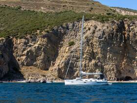 A beautiful sailboat anchored near a rugged coastline, showcasing the serene beauty of the sea and cliffs — perfect for sailing adventures.