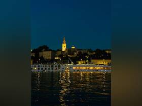 A beautifully illuminated boat glides along the water at night, reflecting the vibrant cityscape in the background — a perfect scene for evening cruises.